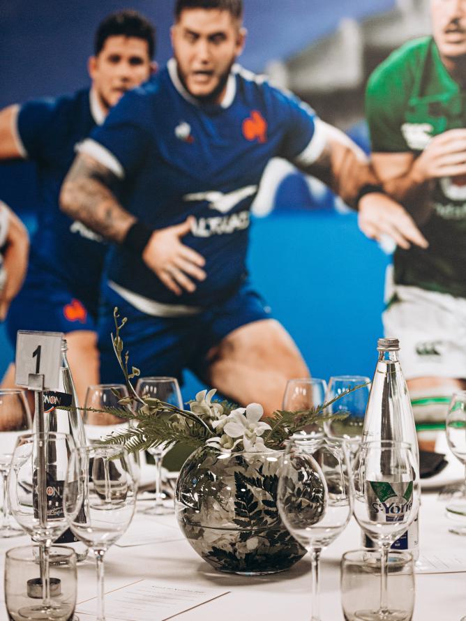 Une table d'un espace hospitalité premium avec en fonds un match de rugby