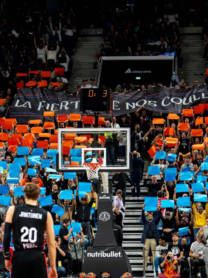 Supporters seated along the court side at the Adidas Arena, cheering for Paris Basketball during an intense EuroLeague match