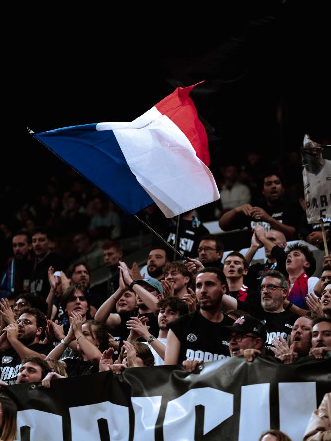 Paris Basketball supporters standing and cheering enthusiastically at the Adidas Arena during a EuroLeague game